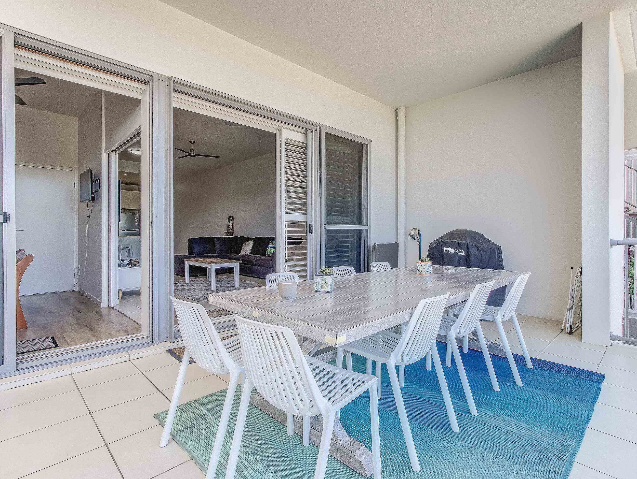 A dining area with a table and chairs, a grill, and a view of a living room with a couch and a television.