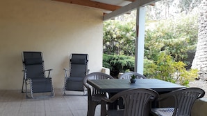 A covered patio area with a table and chairs, a ceiling with wooden beams, and a view of greenery outside. - Studio Bird de mer (Canale-di-Verde)