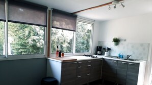 A modern kitchen with wooden cabinets, a gas stove, and a window with a view of greenery. - Studio Bird de mer (Canale-di-Verde)
