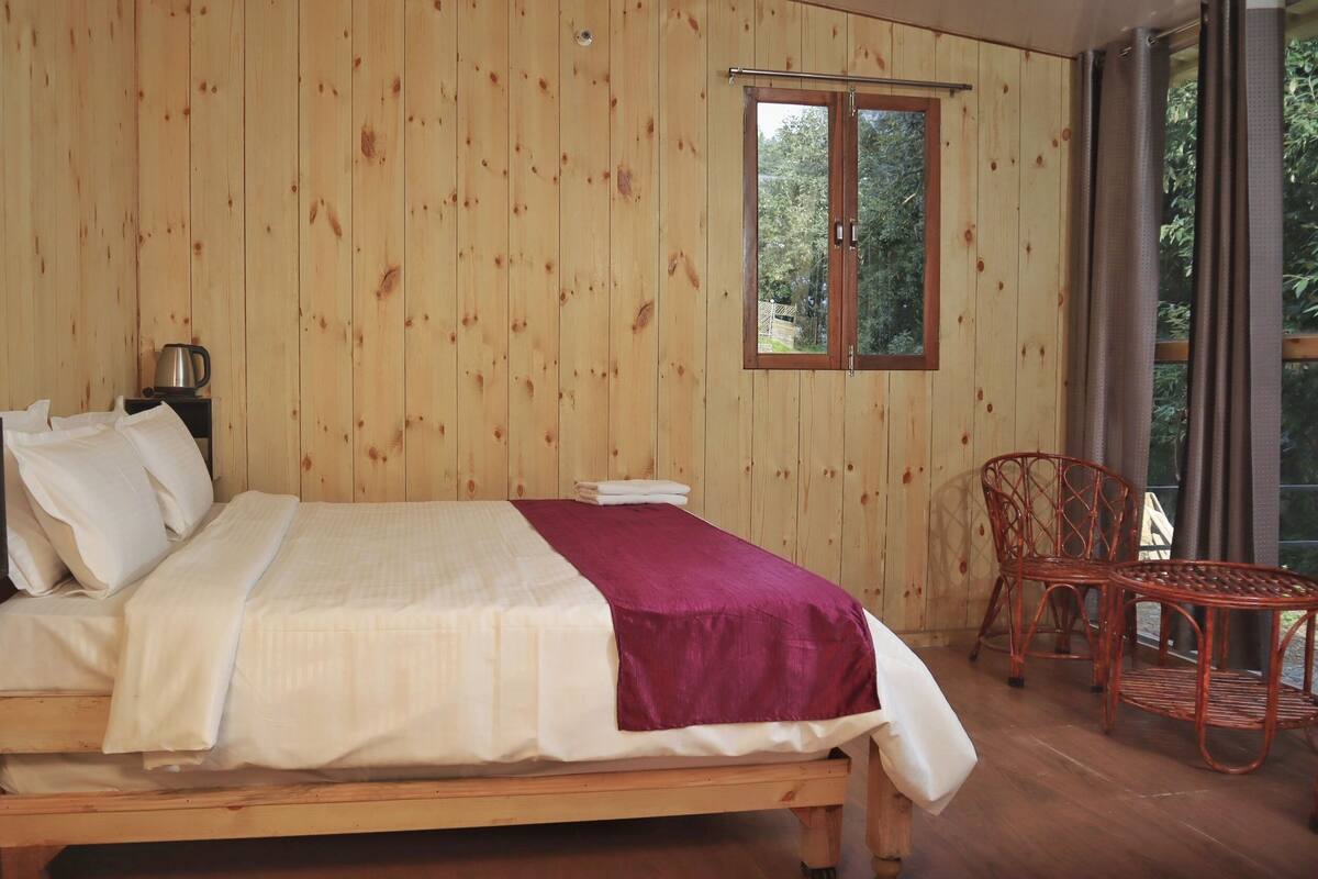 Ein Zimmer mit Holzboden, einem Bett, einem Stuhl, einem Tisch und einem Fenster.