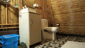 A compact bathroom with a toilet, a small sink, and a cabinet. The walls are covered with bamboo panels, and the floor has a patterned tile design. - Beyond Stay Ananhyam Resort Sattal (Noida)