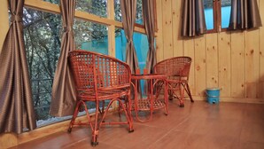 A room with two wicker chairs and a small table, wooden walls, and a window with curtains. - Beyond Stay Ananhyam Resort Sattal (Noida)
