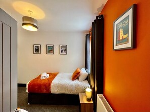 A hotel room with a bed, a nightstand, a wall-mounted picture frame, and a ceiling light fixture.