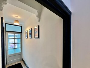 Un couloir avec une porte en verre dépoli, un luminaire suspendu et trois tableaux encadrés accrochés au mur.
