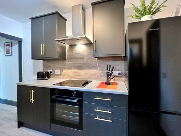 A modern kitchen with black cabinetry, a built-in oven, a stainless steel range hood, and a black refrigerator.