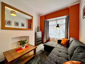 A living room with a sofa, a table with a plant, a mirror, and a window with curtains.