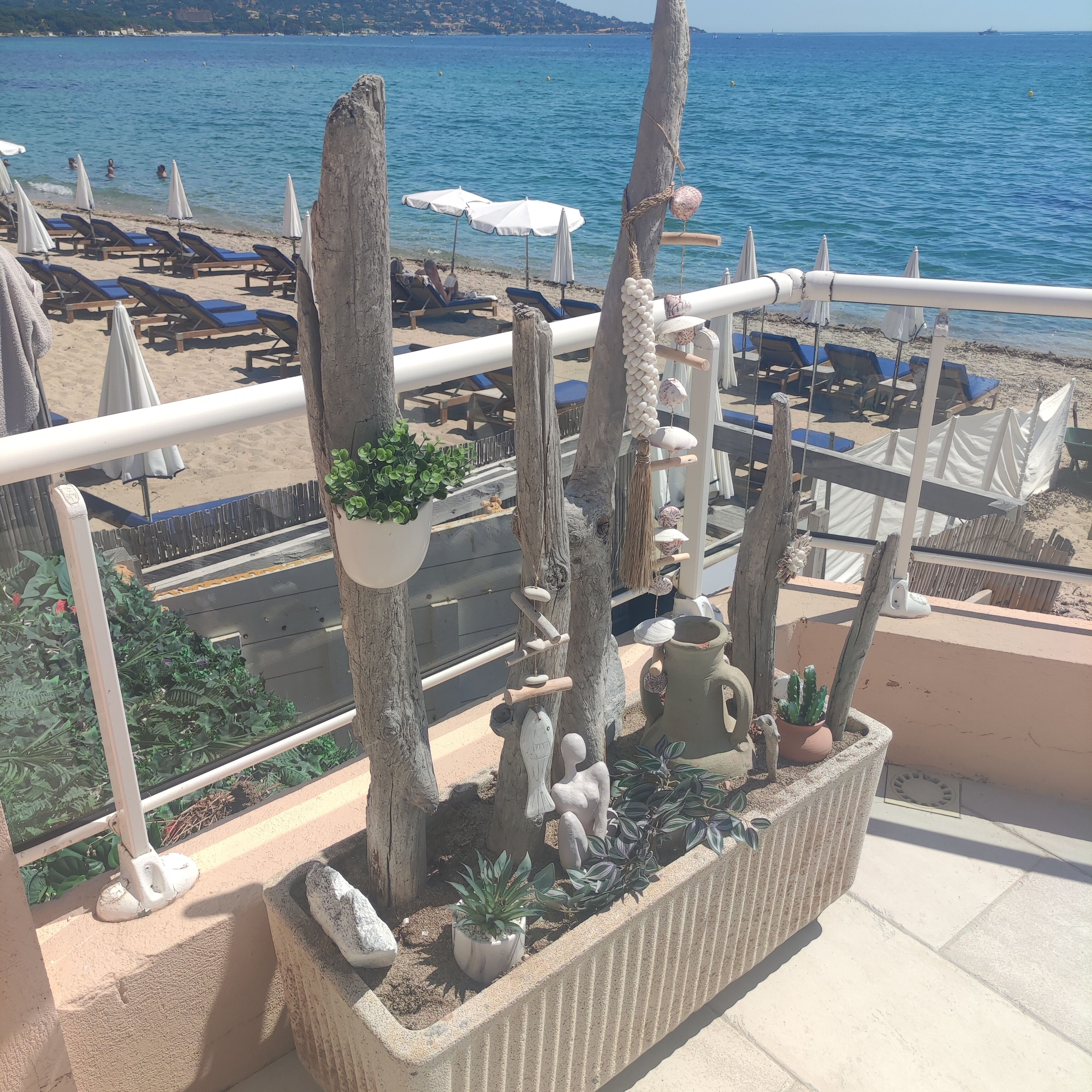 Un balcone con vista sul mare, con poltrone relax, ombrelloni e piante ornamentali.