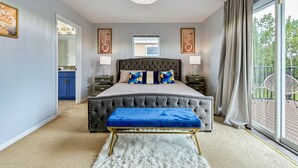 A bedroom with a large bed, a chandelier, a view of the outdoors, and a bathroom with a blue cabinet. - Beautiful Family Getaway Davenport Florida (Davenport)