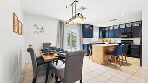 A modern kitchen with dark cabinets, a central island, and a dining area with a table and chairs. - Beautiful Family Getaway Davenport Florida (Davenport)