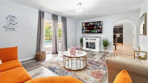 A modern living room with a fireplace, a bookshelf, and a large window with curtains. - Beautiful Family Getaway Davenport Florida (Davenport)
