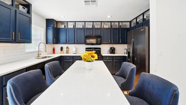 A modern kitchen with dark blue cabinets, a central island with a vase of sunflowers, and a stainless steel refrigerator. - Beautiful Family Getaway Davenport Florida (Davenport)