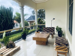 A balcony with a wooden table and two patterned sofas, surrounded by potted plants and a metal railing. - Affordable Homes Kigali (Kigali)