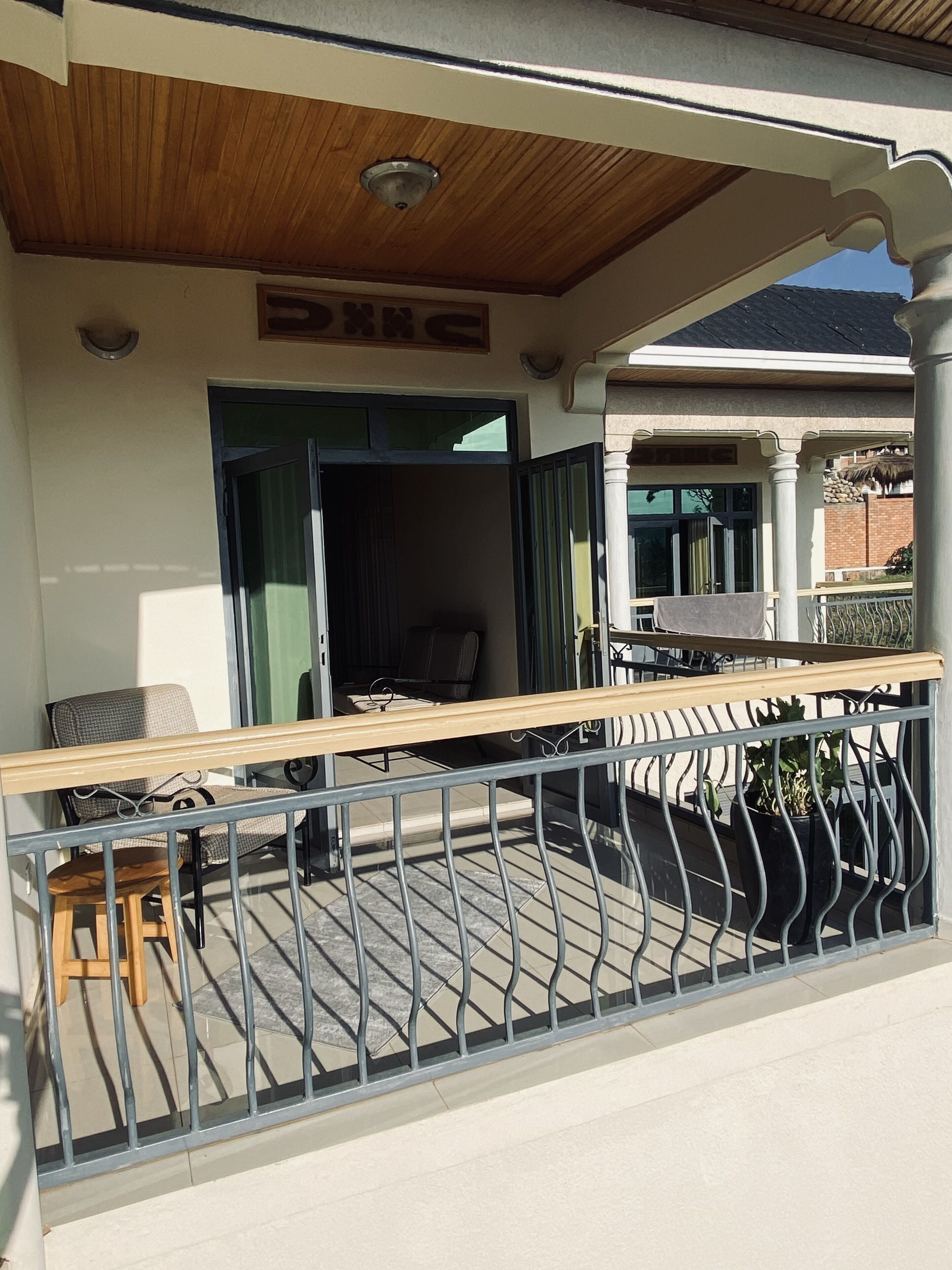 A covered outdoor seating area with a wooden bench and chairs, a metal railing, and a view of the street.