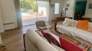 Ein geräumiges Wohnzimmer mit einem großen Schiebeglasfenster, das zu einem Außenbereich mit Pool und Liegestühlen führt.