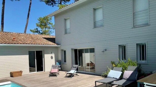 Ein zweistöckiges Haus mit Swimmingpool, einer Terrasse mit Liegestühlen und einem überdachten Außenbereich.