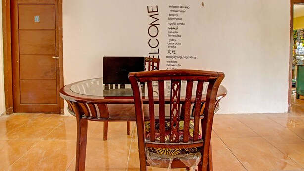 A reception area with a wooden door, a glass table, and a chair. A welcome sign with multiple languages is on the wall. - Hotel O Kedai Cinta Guest House (West Cirebon)