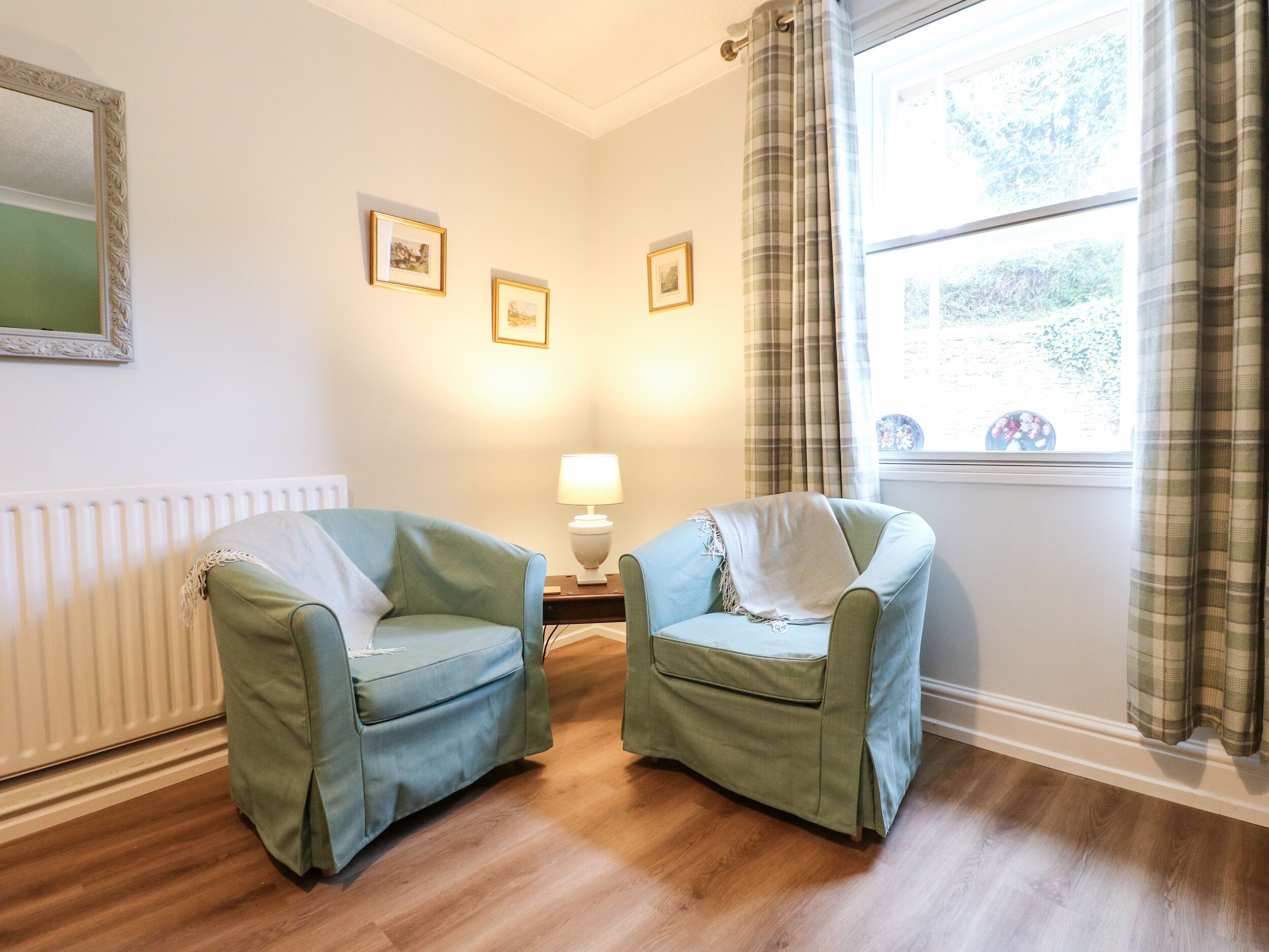 A room with two armchairs, a radiator, a lamp, and framed pictures on the wall.