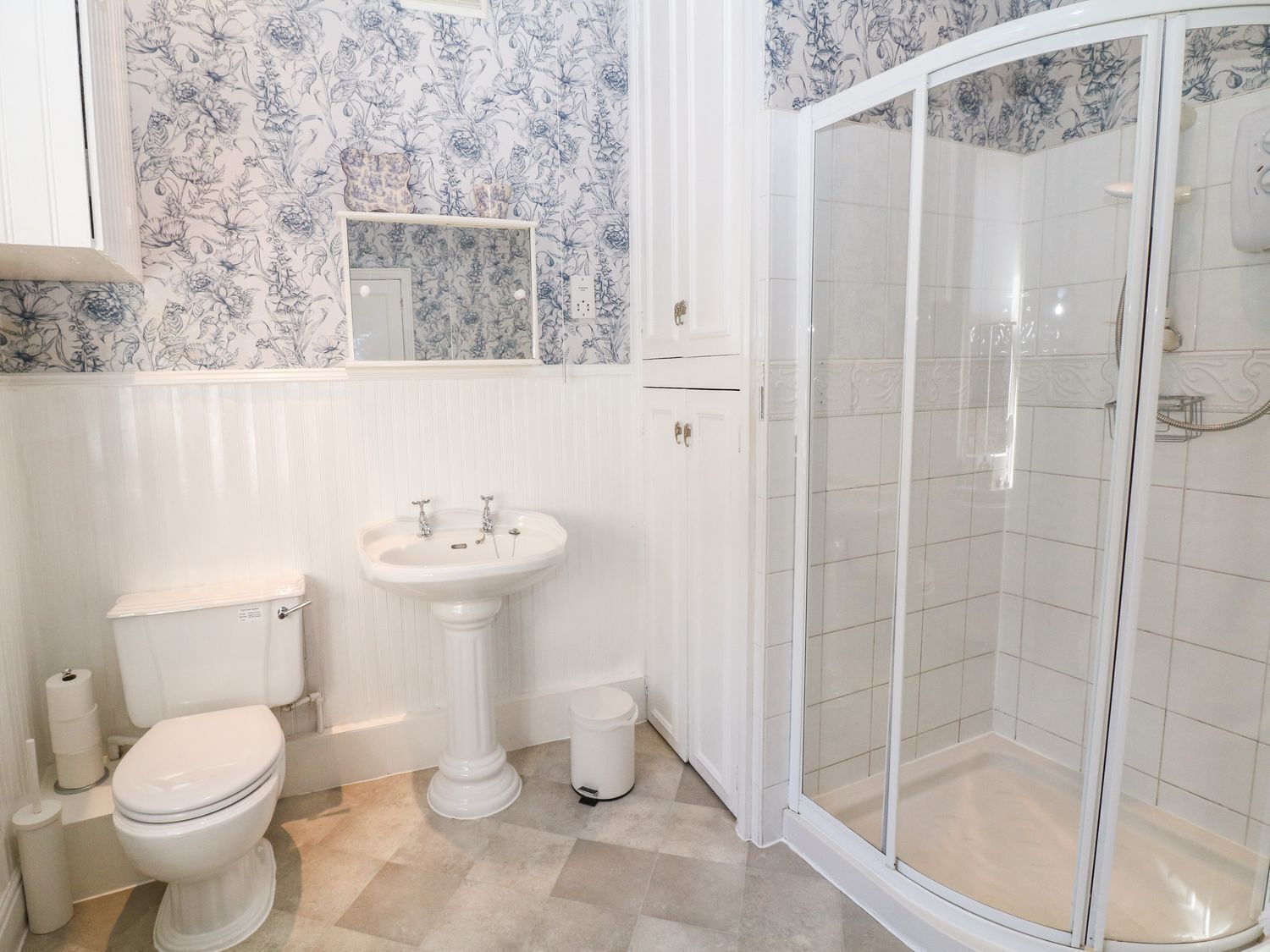 A bathroom with a toilet, pedestal sink, and a glass-enclosed shower.