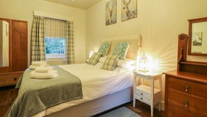 A bedroom with a bed, bedside table, dresser, and artwork on the wall. - Knoll Cottage (Bakewell)