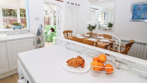 Een moderne keuken met witte kasten, een groot eiland met een fruitmand, en een eetgedeelte met een houten tafel en stoelen.