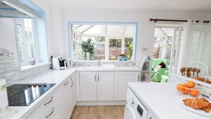 Een moderne keuken met witte kasten, een ingebouwde oven, een wasmachine en een raam met uitzicht op een tuin.