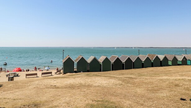 Een strand met groene strandhutten, een zandvlakte met banken en de zee op de achtergrond.