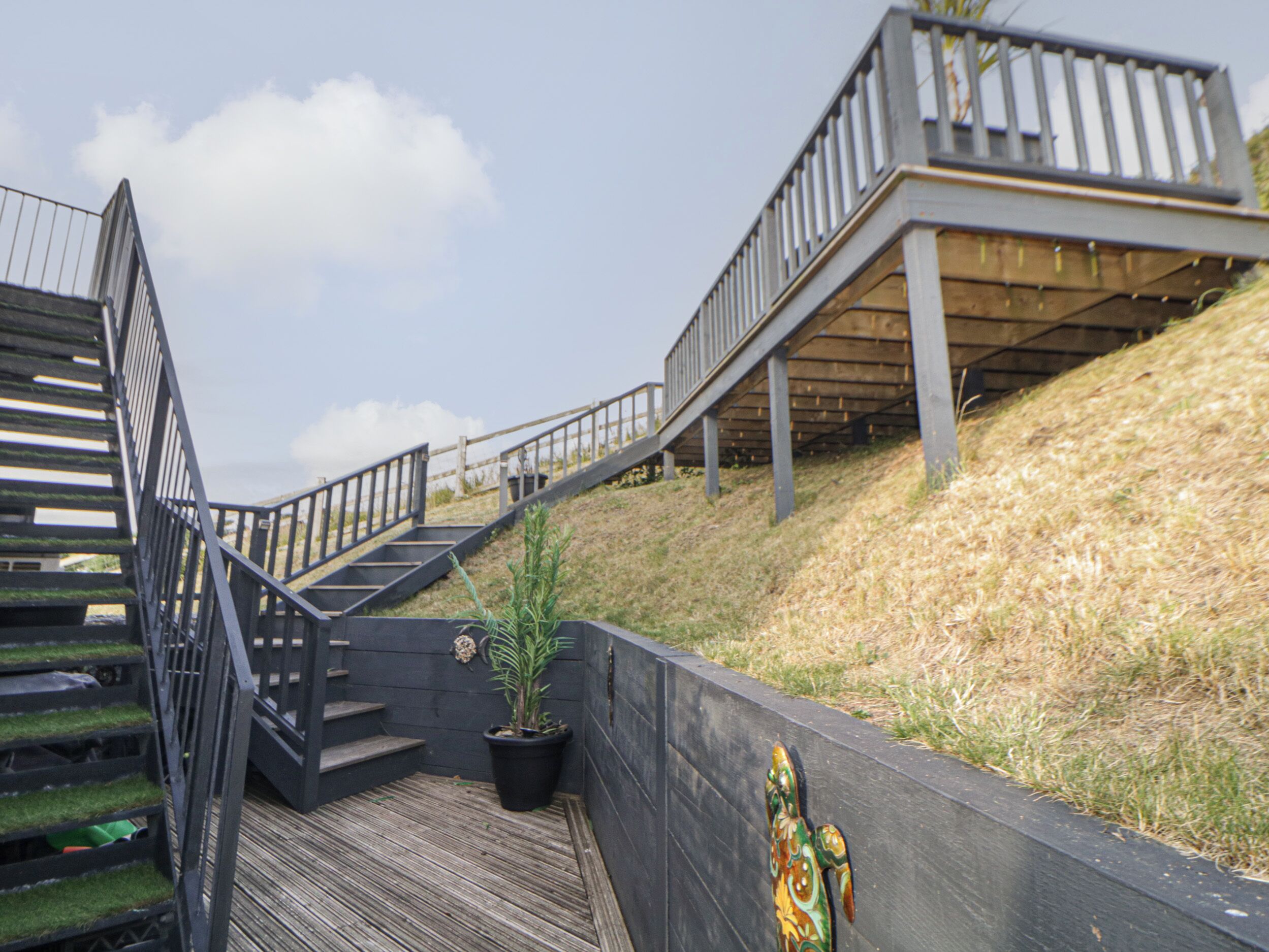 Una escalera de madera con barandillas metálicas que asciende por una ladera cubierta de hierba.