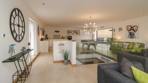 Una sala de estar moderna con un sofá gris, una mesa de centro y un sillón verde. Se ve un área de cocina con una mesa de comedor y sillas al fondo.