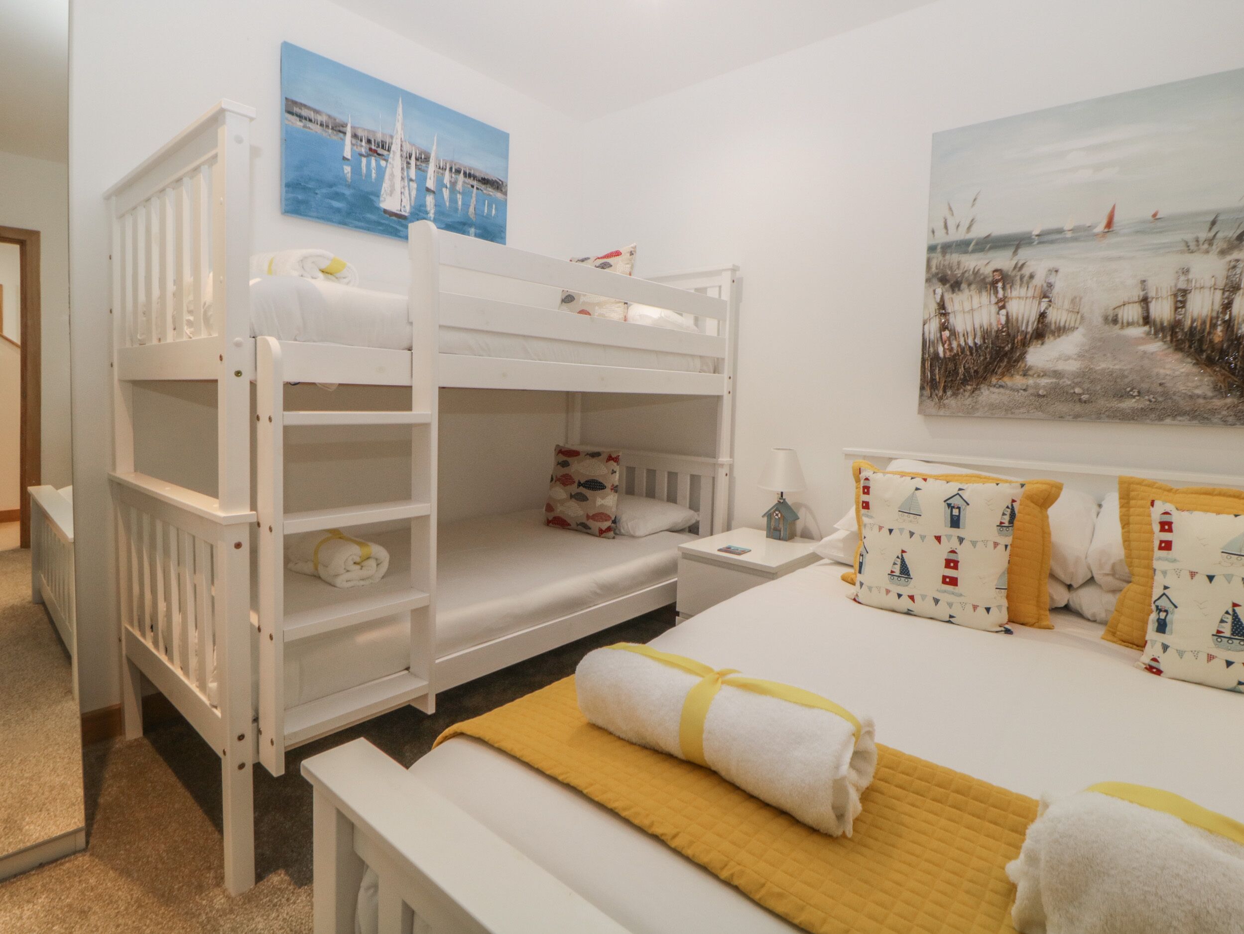 A child’s bunk bed with a small desk and chair, a bedside table with a lamp, and a bed with a yellow blanket and pillows.