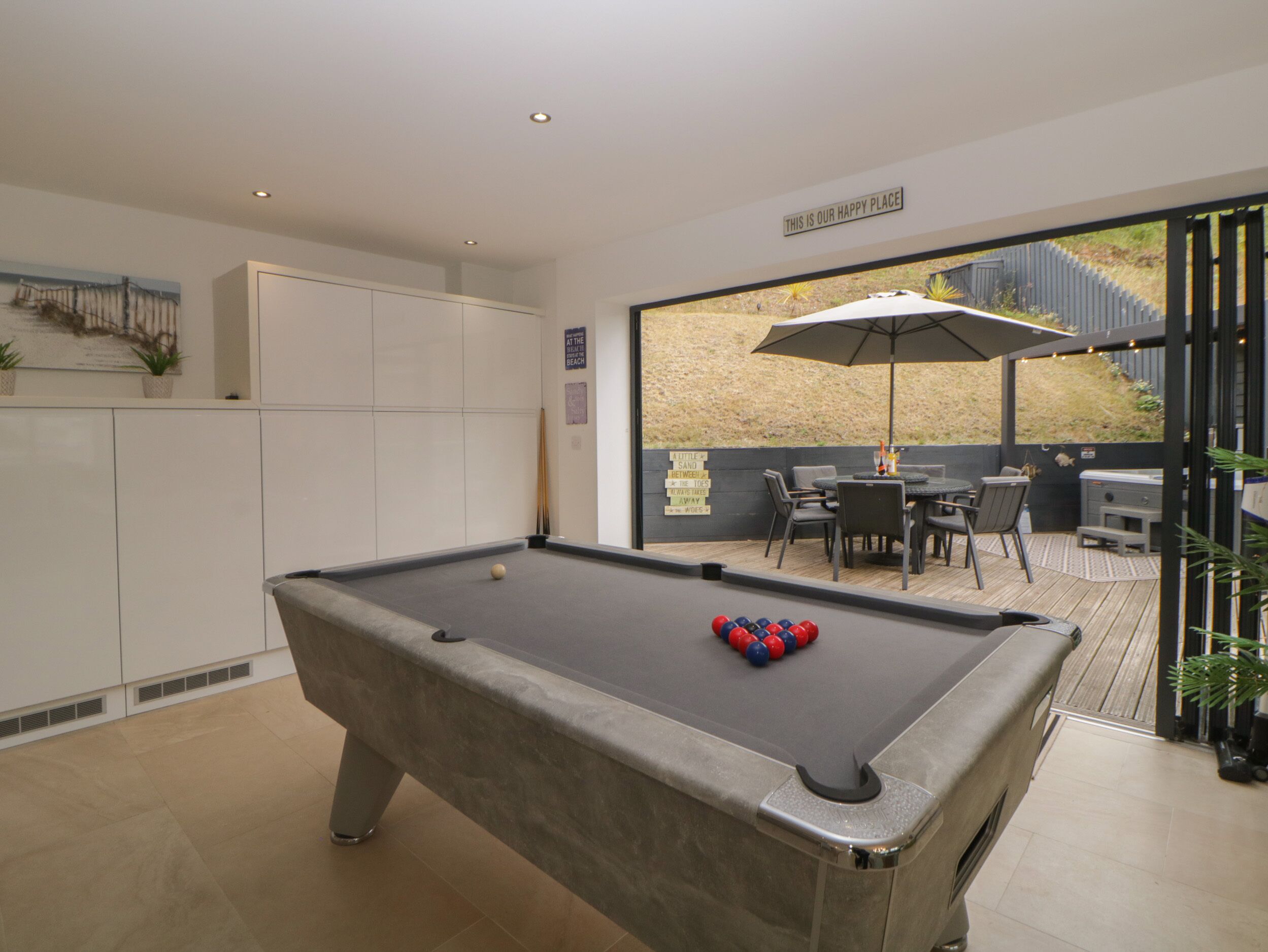 A pool table with balls, a seating area with chairs and an umbrella, and a view of the outdoors.