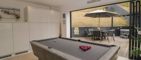 A pool table with balls, a seating area with chairs and an umbrella, and a view of the outdoors.