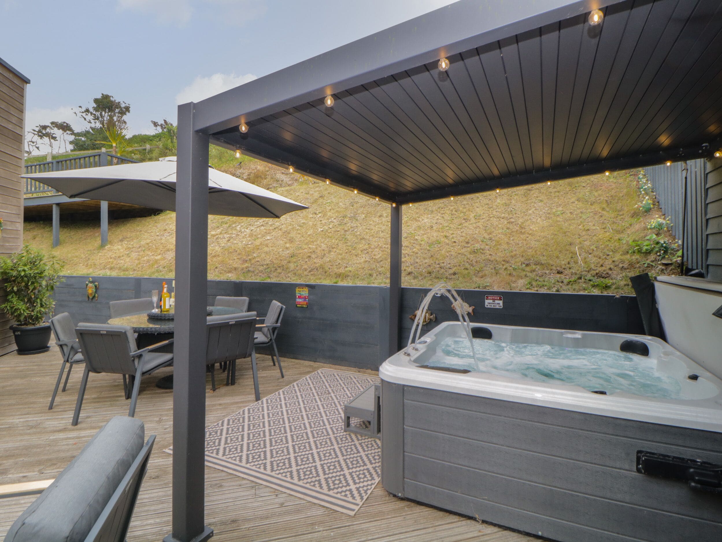 Un espacio al aire libre cubierto con un jacuzzi, asientos y una pérgola con luces colgantes.