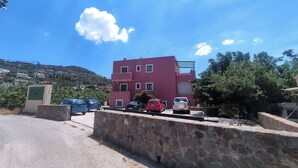 A red building with a stone wall in front, parked cars, and a clear blue sky. - Quiet apartment in Marathonas - 5 min from the beach! (Μαραθώνας)