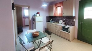 A compact kitchen with a dining table, chairs, a refrigerator, a microwave, and a green door. - Quiet apartment in Marathonas - 5 min from the beach! (Μαραθώνας)