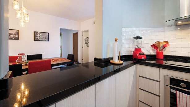 A modern kitchen with a black countertop, a red blender, and a dining area with red chairs and a wooden table. - Casa de Chiles - the best spot in Cuauhtémoc (Mexico City)