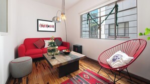 A modern living room with a red sofa, a small Christmas tree, a red chair, and a large window with a view of the outside. - Casa de Chiles - the best spot in Cuauhtémoc (Mexico City)