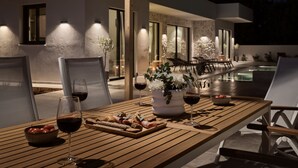 Un espace extérieur aménagé pour les repas, avec une table en bois, des chaises et une piscine en arrière-plan.