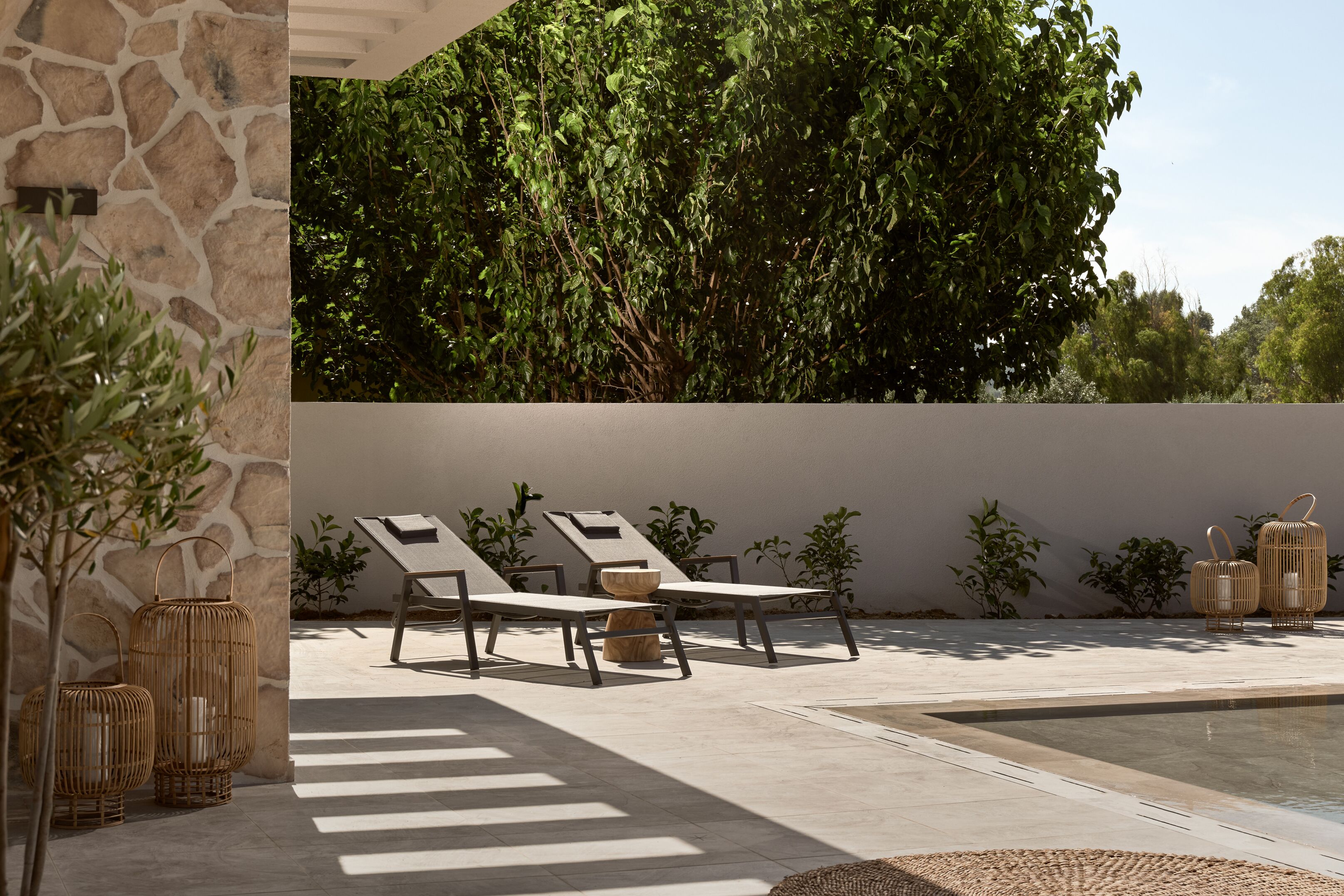 A sunlit outdoor seating area with lounge chairs and a stone wall backdrop.