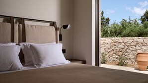 Une chambre à coucher avec un lit, des oreillers, une table de chevet, une lampe et une vue sur un mur de pierre et la verdure à l’extérieur.