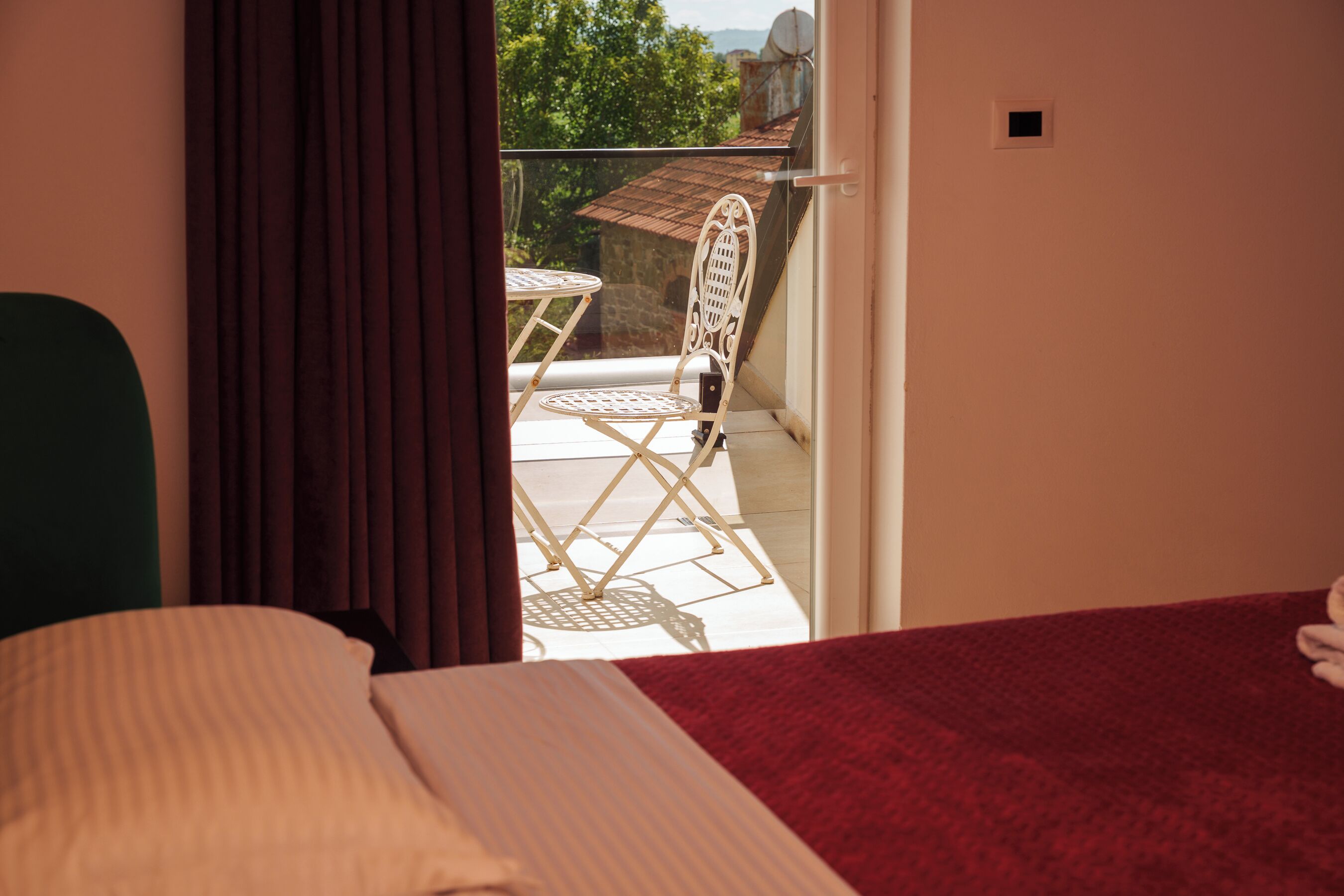 Een kamer met een bed, een rode deken, een witte stoel en een balkon met een tafel en stoel.