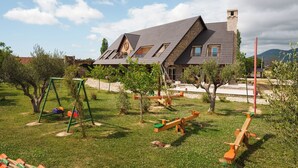 Une maison avec un toit en pente, une cheminée et un jardin équipé de balançoires et de jeux à bascule.