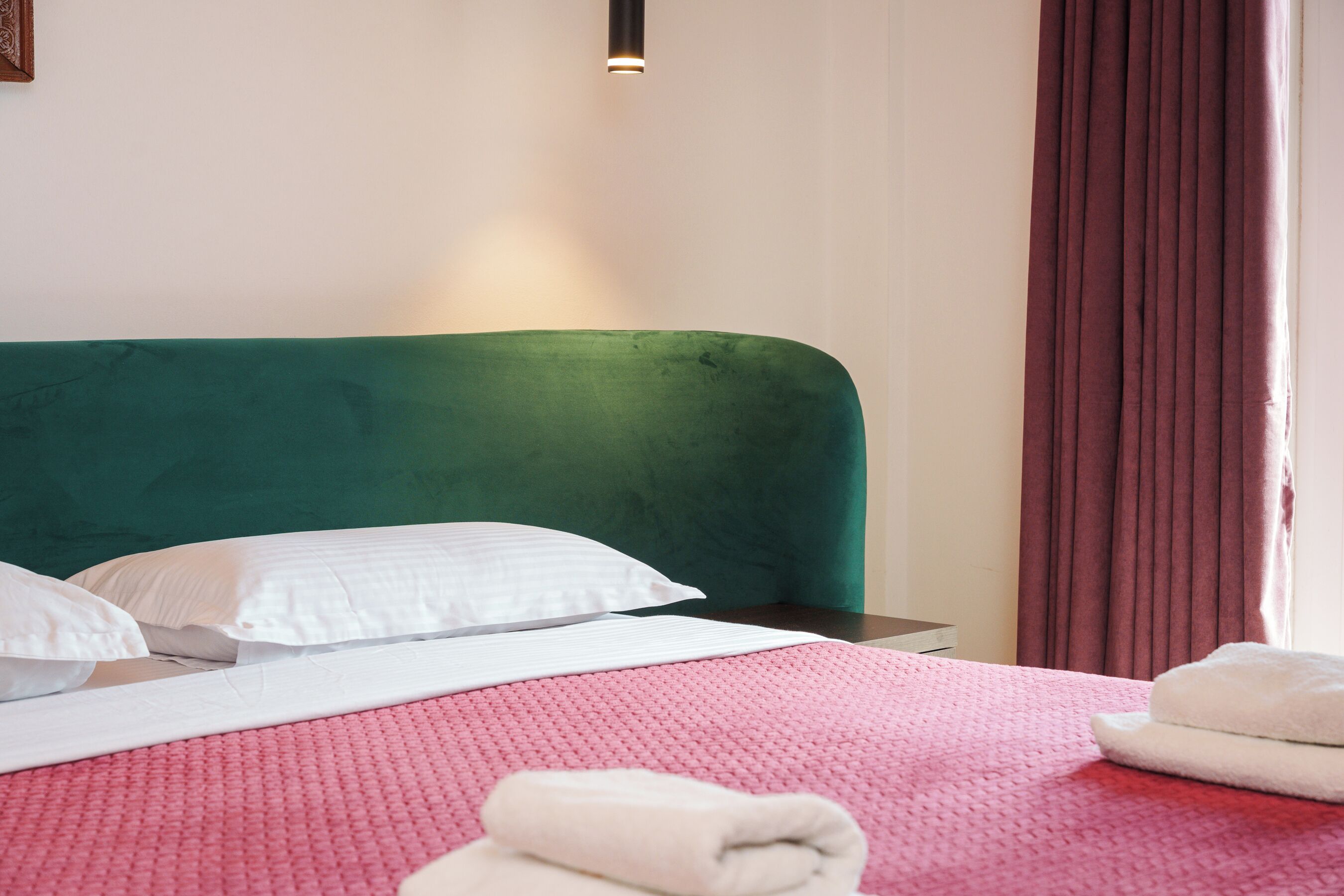 Un letto rifatto con ordine, con una testiera verde, cuscini bianchi e una coperta trapuntata rosa.