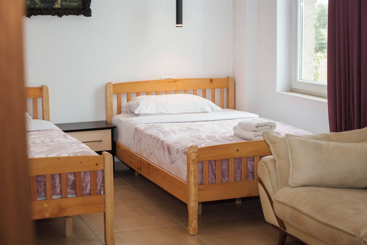 Habitació amb dos llits de fusta, un escriptori petit, una cadira amb coixí i una finestra amb cortines.