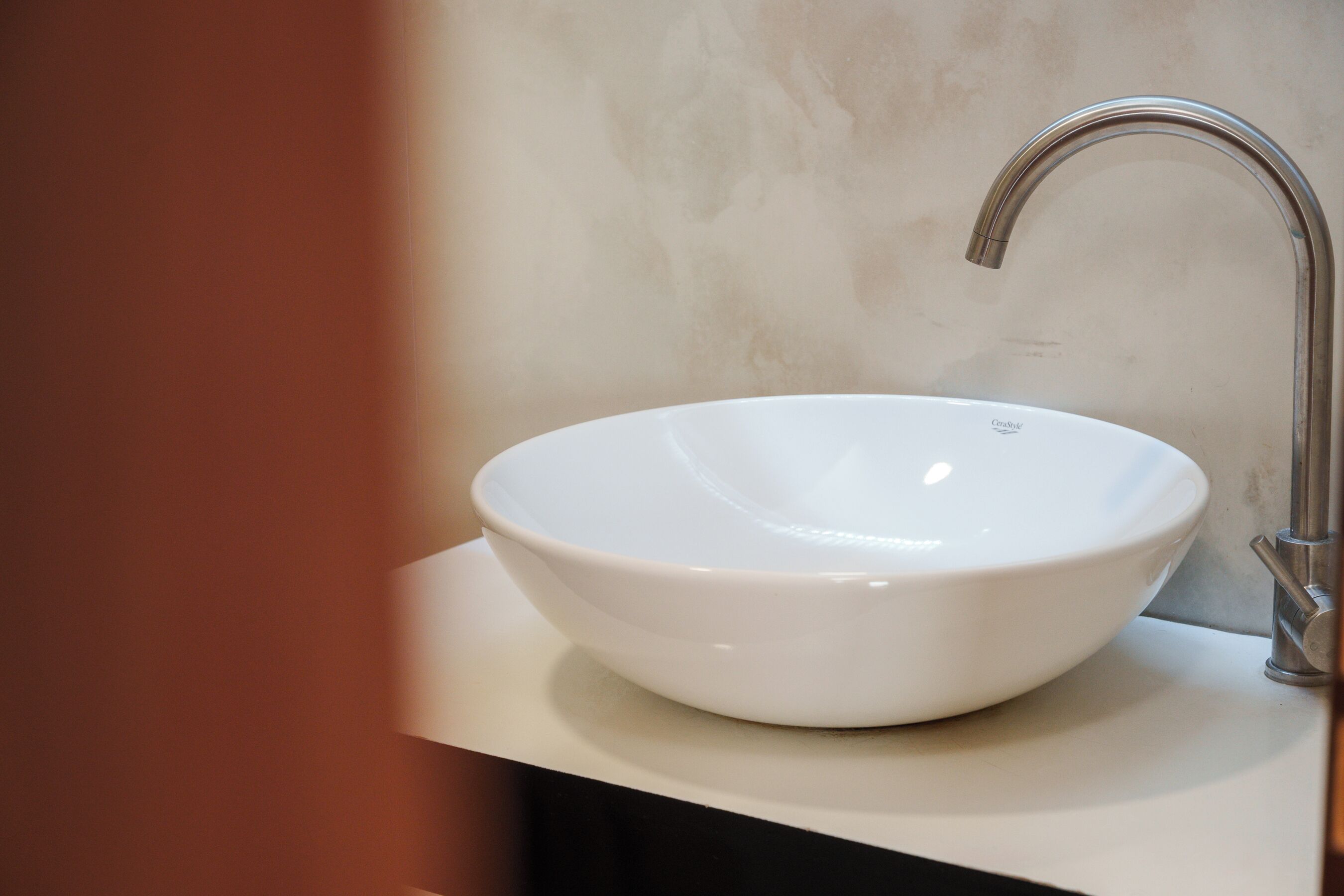 Un lavandino di ceramica bianca con un solo rubinetto su un piano di lavoro bianco.