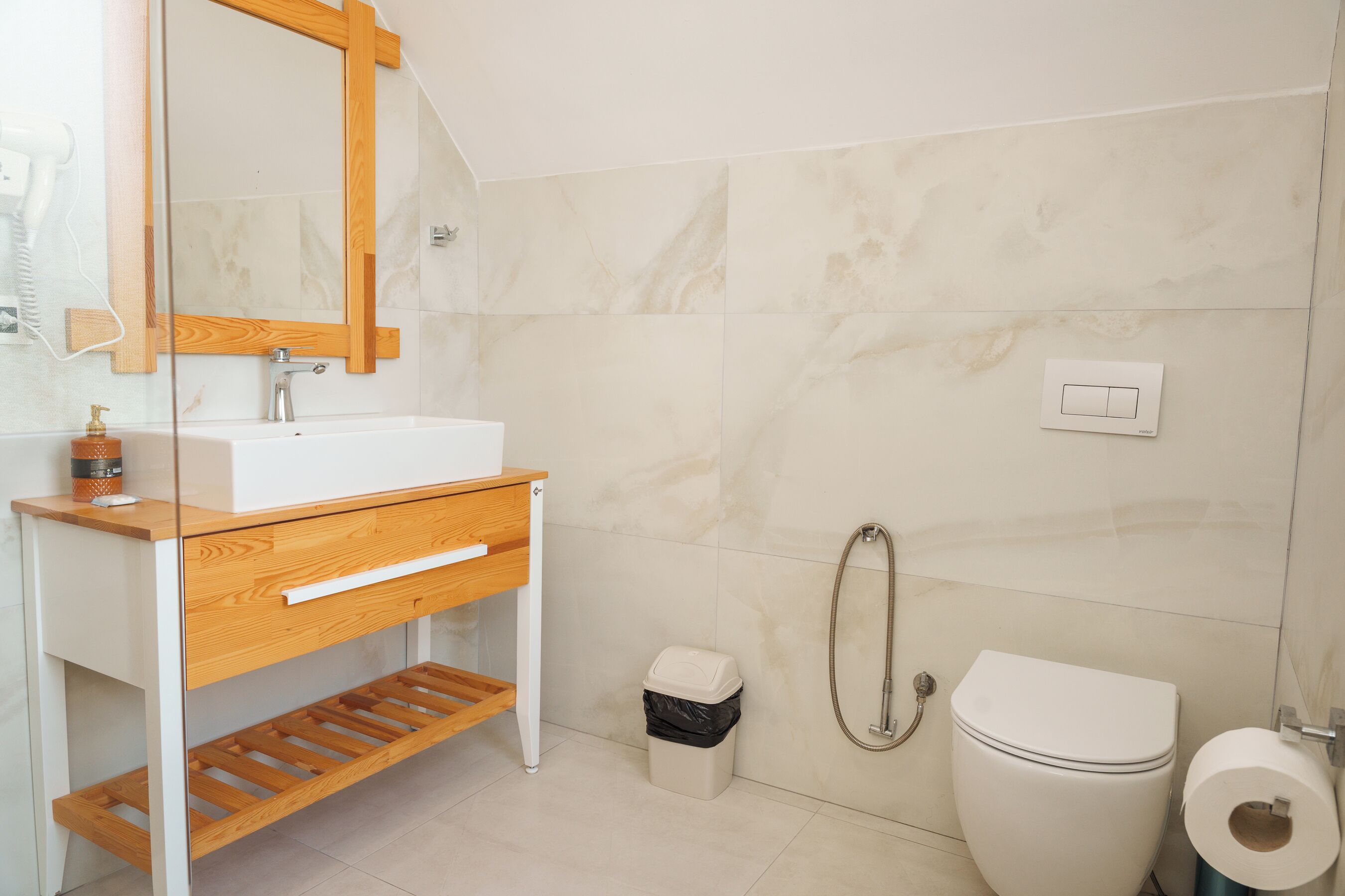 Un baño con tocador de madera, lavamanos blanco, inodoro y ducha.