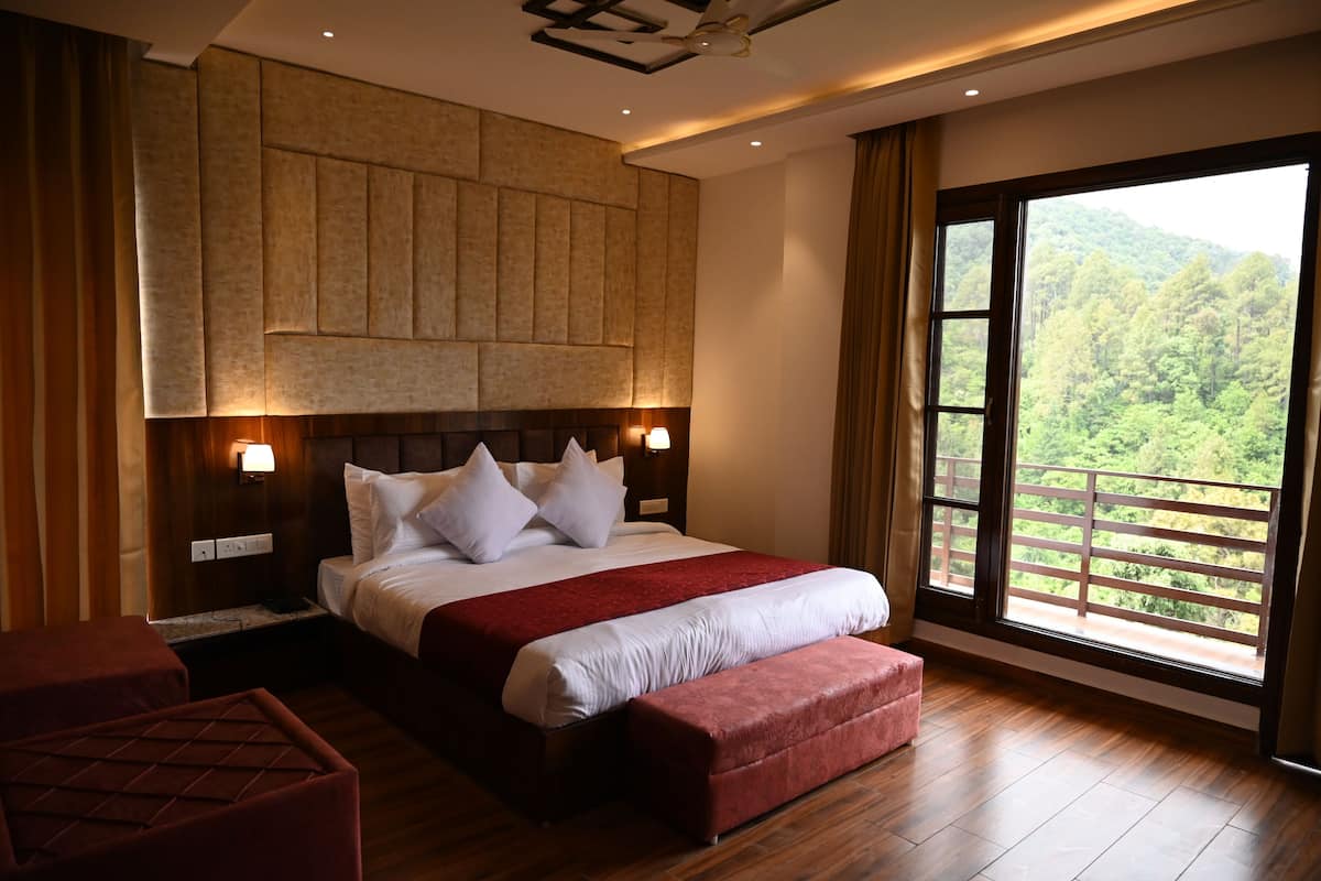 Ein Hotelzimmer mit einem großen Bett, einem hölzernen Kopfteil, einer roten Bank und einem Balkon mit Blick auf Grünflächen.