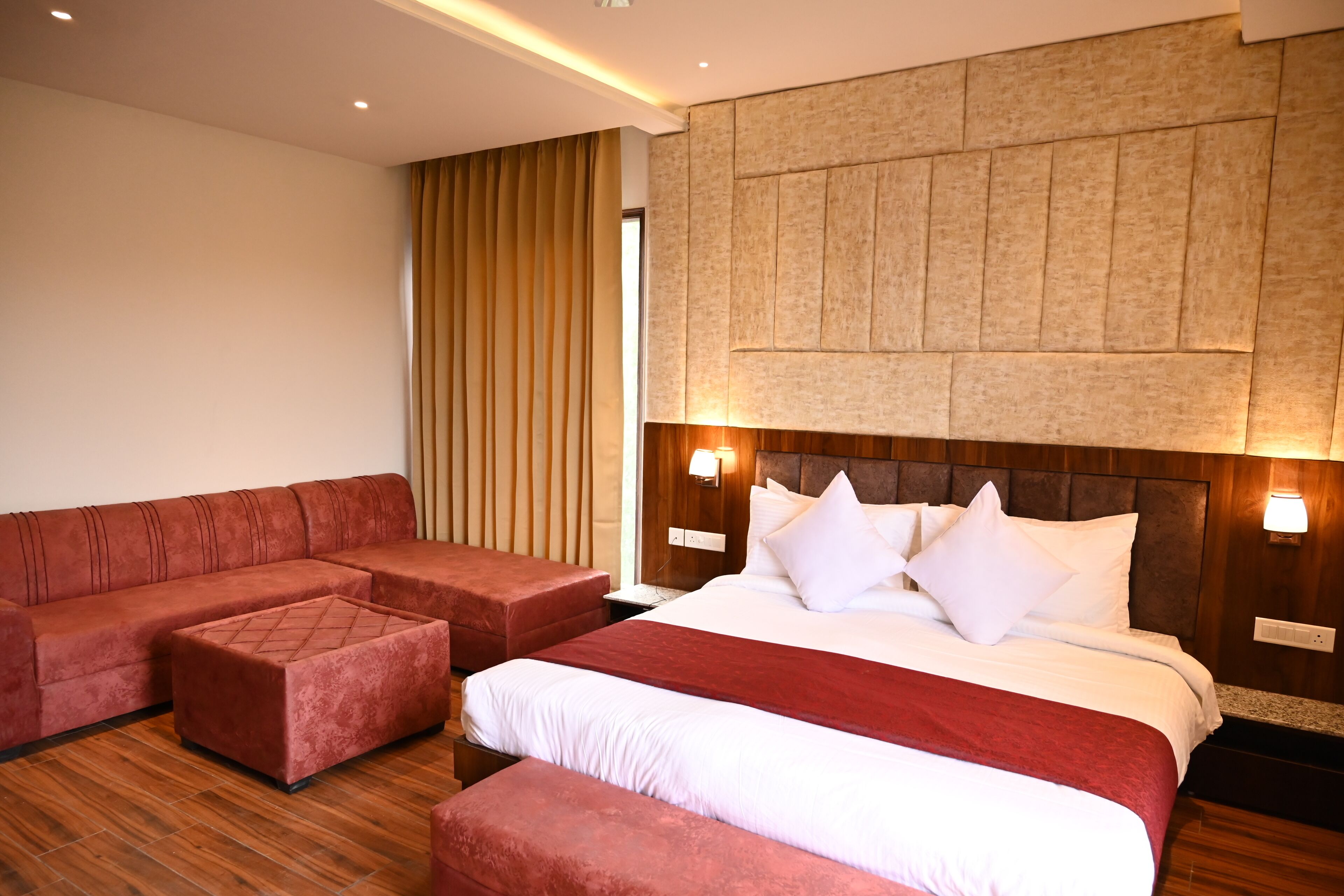 A hotel room with a large bed, a red sofa, and a wooden floor.
