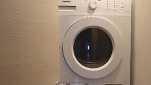 A laundry room with two stacked washing machines, a control panel, and a door. - Vrbo Property (Gorizia)