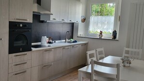 A modern kitchen with light wood cabinetry, a built-in oven, and a window with a view of greenery. - Vrbo Property (Gorizia)