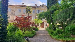 A traditional building with a gravel pathway leading to a wooden door, surrounded by lush greenery and trees. - Vrbo Property (Gorizia)